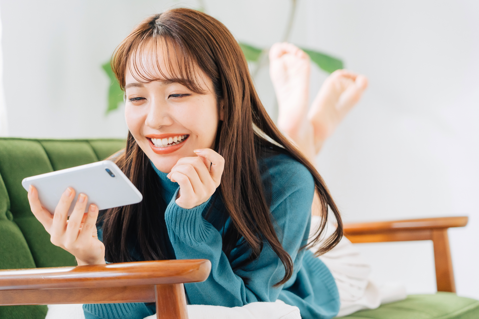 ソファでくつろぎながらスマートフォンを見る女性のイメージ
